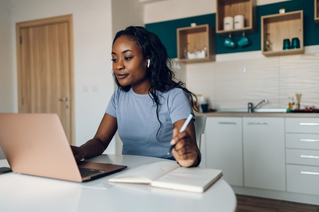 Young african american woman making video call with laptop in a kitchen at home and having an online web conference with her colleagues from work Social distance and modern technology